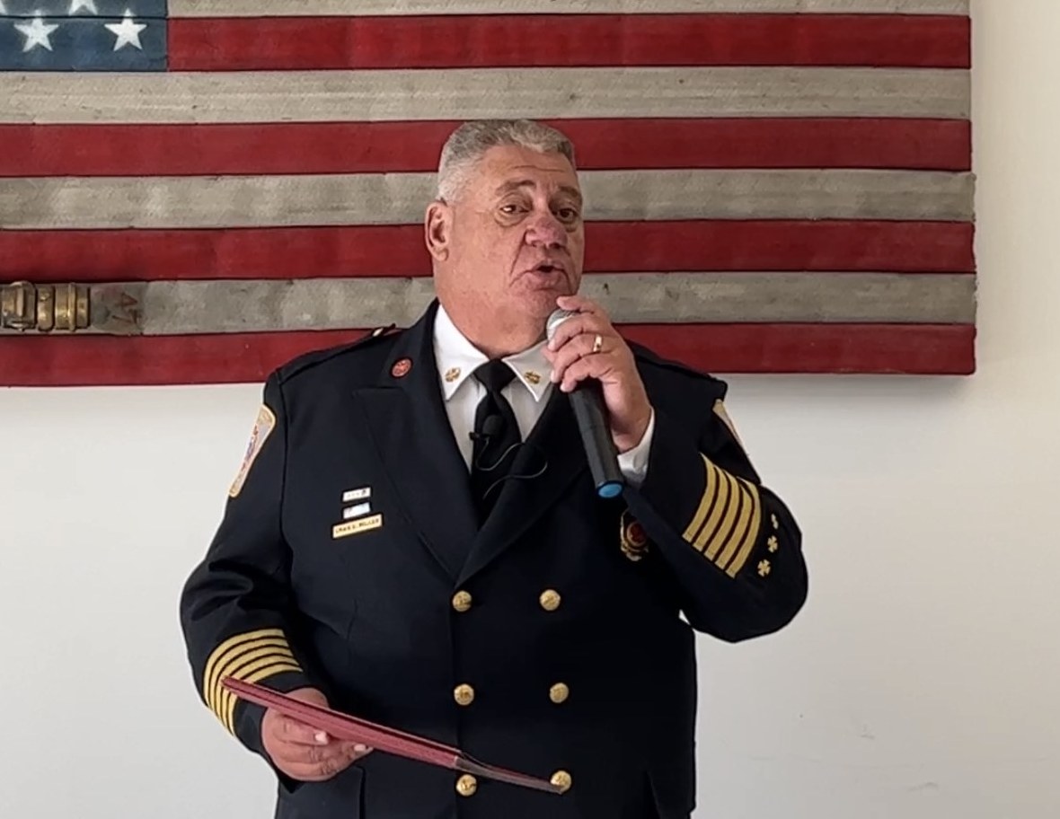 Fire Chief Craig Miller in dress uniform addressing the Open House crowd beneath the American flag